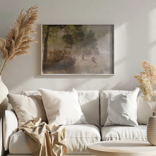 Two geese flying low over a misty forest lake at dawn, a serene nature photograph.