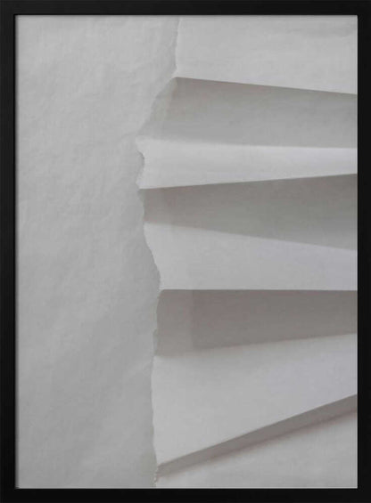 A minimalist composition of folded and torn white paper, showcasing geometric forms and shadows in a black frame.