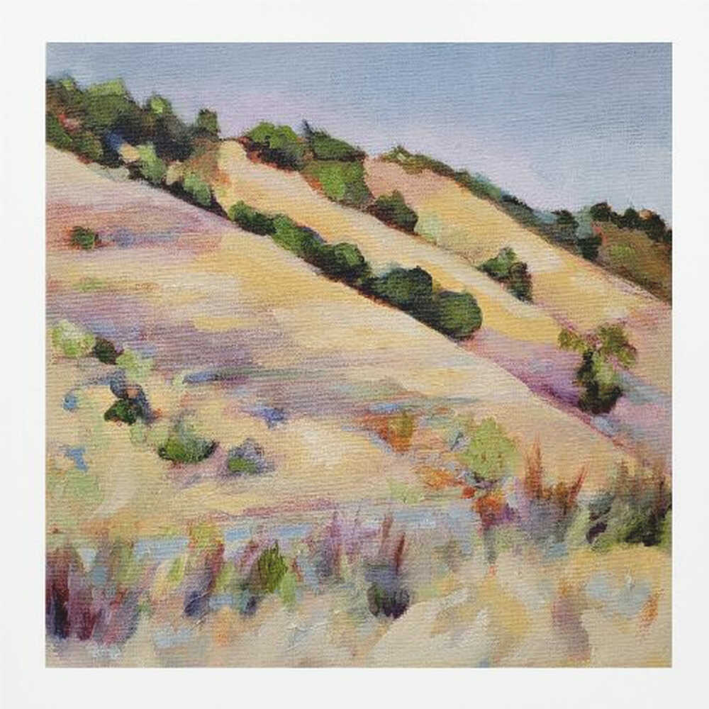 An impressionist oil painting of golden, rolling hills dotted with green shrubs under a pale blue sky, framed in light wood.