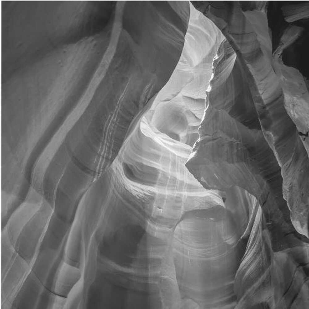 Black and white photo of light in a narrow slot canyon, highlighting smooth, layered rock formations. Nature wall art.