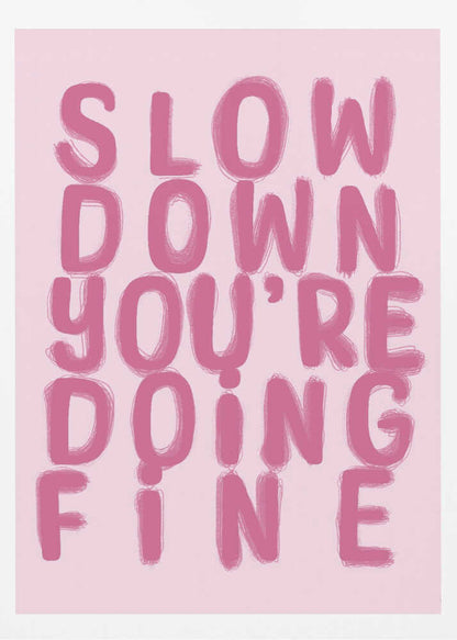 A framed art print featuring the phrase 'SLOW DOWN YOU'RE DOING FINE' in a bold, dark pink, brush-stroke font. The words are stacked vertically against a light pink background, all enclosed within a simple black frame. Artwork