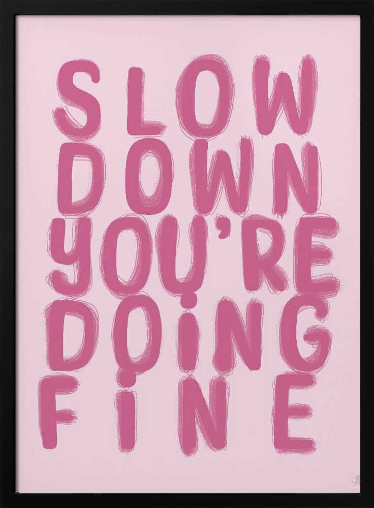A framed art print featuring the phrase 'SLOW DOWN YOU'RE DOING FINE' in a bold, dark pink, brush-stroke font. The words are stacked vertically against a light pink background, all enclosed within a simple black frame. Artwork
