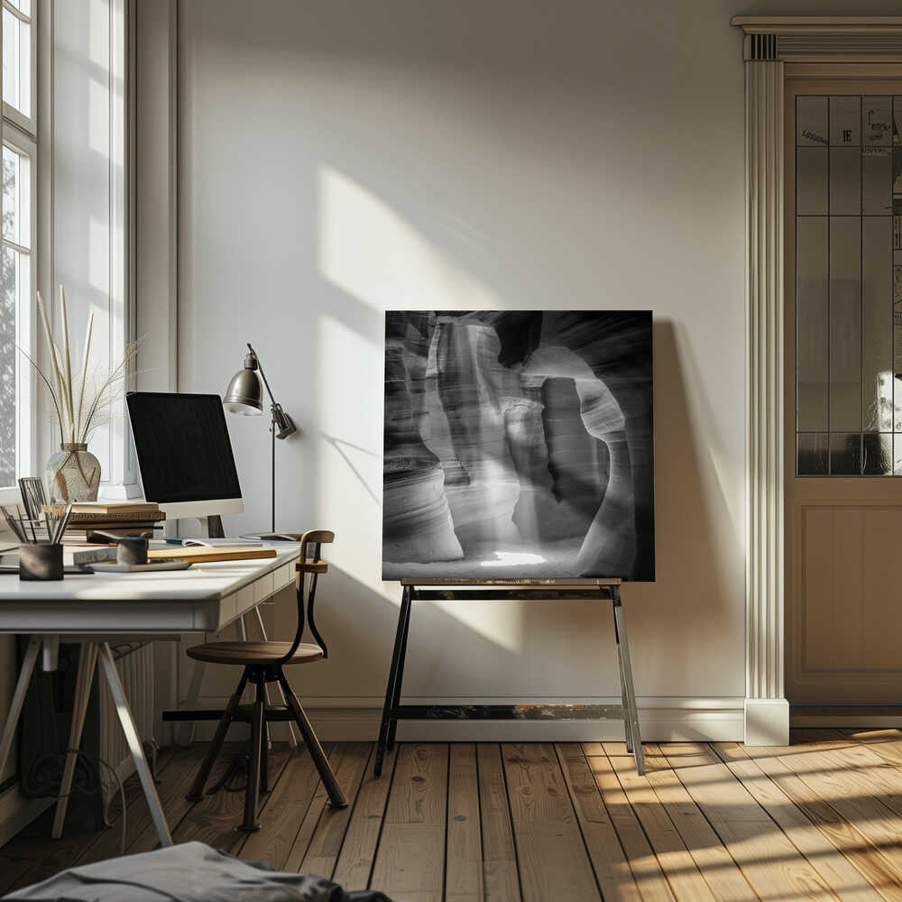 A dramatic black and white photo of a sunbeam lighting the sandy floor of a smooth, curved slot canyon.