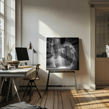 A dramatic black and white photo of a sunbeam lighting the sandy floor of a smooth, curved slot canyon.