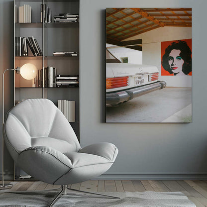 A film-style photograph showing the rear of a classic white Mercedes-Benz parked under a carport with exposed wooden beams. On the adjacent white wall hangs a vibrant red pop-art portrait of a woman with dark hair. Artwork