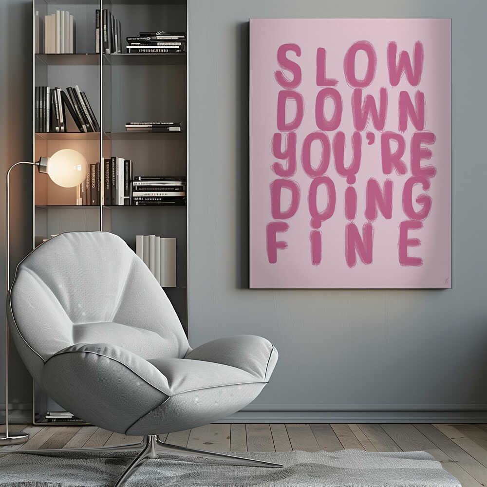 A framed art print featuring the phrase 'SLOW DOWN YOU'RE DOING FINE' in a bold, dark pink, brush-stroke font. The words are stacked vertically against a light pink background, all enclosed within a simple black frame. Artwork