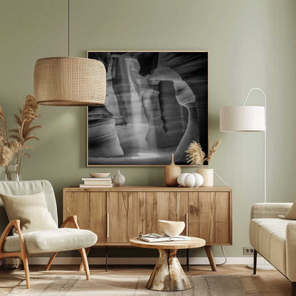 A dramatic black and white photo of a sunbeam lighting the sandy floor of a smooth, curved slot canyon.