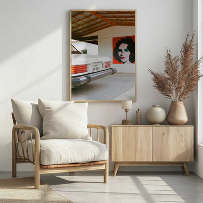 A film-style photograph showing the rear of a classic white Mercedes-Benz parked under a carport with exposed wooden beams. On the adjacent white wall hangs a vibrant red pop-art portrait of a woman with dark hair. Artwork